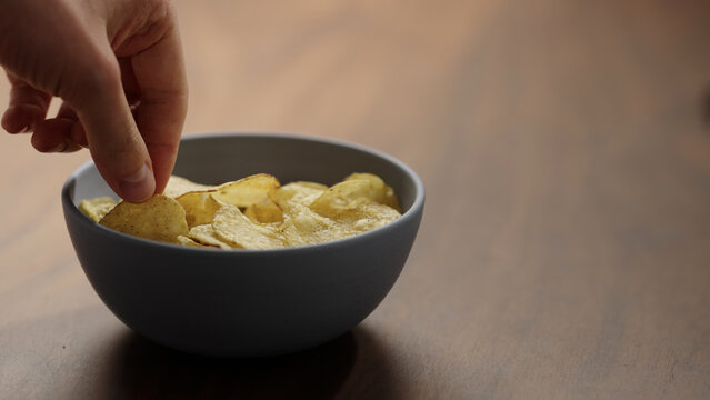 Close-up of man hand take potato chips in a ceramic bowl on wooden table