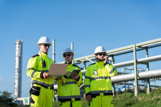 Team of engineers working at oil and gas refinery, Industrial engineers with laptop and tablet inspecting oil refinery site, Group of plant operators in safety uniforms monitoring oil and gas facility