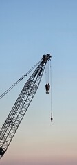 Vertical silhouette of a construction crane boom with hook against a pastel sunset sky, industrial machinery background with copy space, real estate development concept © Наталья Хван