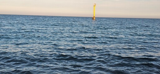 Yellow ocean buoy navigation tower standing in the open sea at sunset, calm blue water with horizon, maritime safety and shipping concept © Наталья Хван