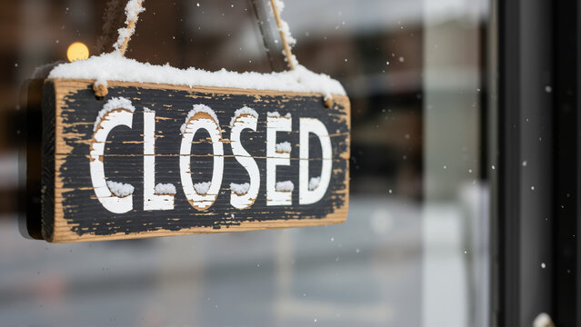 Close up of a wooden closed sign hanging on a shop window in winter. Business closed during snowy weather