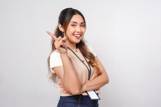 Cheerful young Asian woman in a brown shirt pointing to the copy space behind her.
