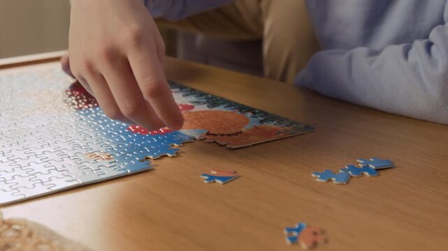 Cropped shot of unrecognizable senior man and child assembling jigsaw puzzle together at wooden table. Footage is ideal for family bonding campaigns or cognitive health advertisements