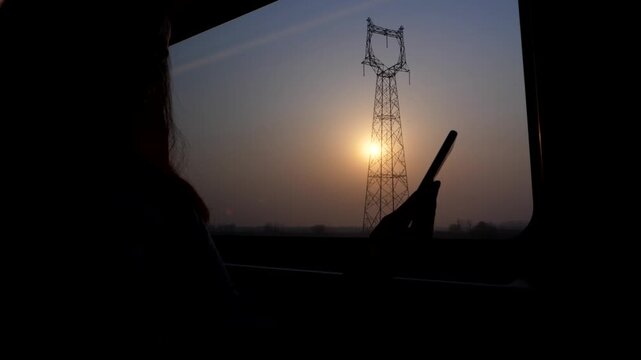 Woman sitting against window at high speed train to Beijing, watch smartphone. Silhouetted slow motion shot of passenger hand holding mobile device. Low sun shine through smoggy air