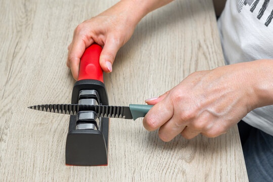 A housewife sharpens a kitchen knife. knife sharpening process. sharpening a kitchen knife in the home kitchen. manual sharpener for a kitchen knife. sharpen a knife. manual knife sharpener