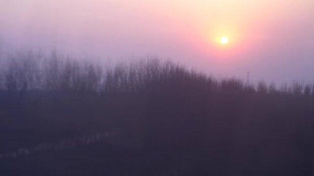 Vivid sun on milky sky, POV look out from high speed train, rural outdoors passed by, slow motion shot. Water channel with sunlight reflection, row of naked trees flick outside