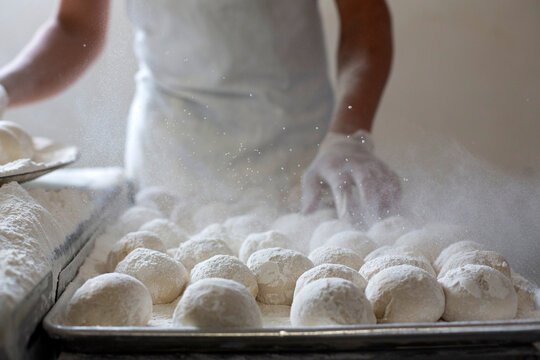 Baker dusting flour over fresh dough balls