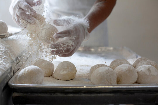 Baker with gloves dusting flour over fresh dough balls