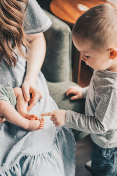 A boy points at his new baby sibling's tiny feet while standing by mom