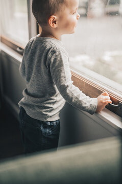 Curious toddler boy standing by the window looking outside