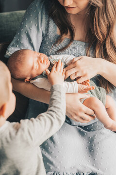 Toddler gently touching sleeping newborn in mother's arms