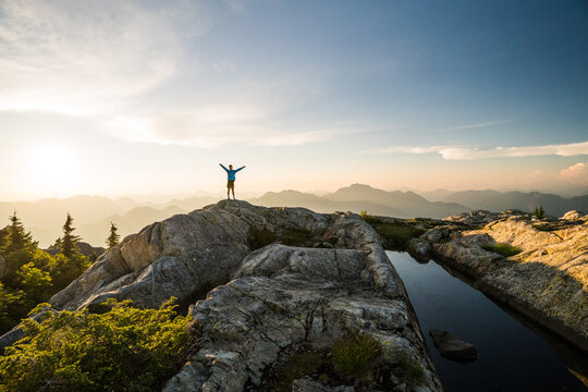Hiker with arms raised on mountain summit at sunset