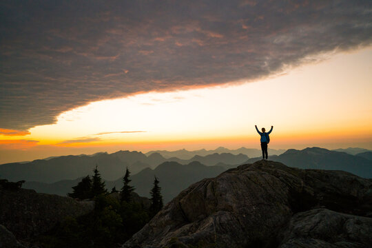 Hiker celebrating on a mountain summit at sunset