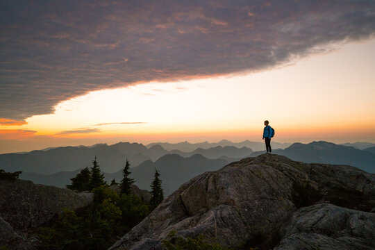 Young boy watches sunset over layered mountains