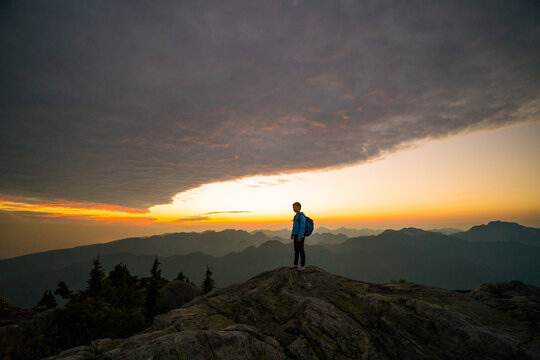 Hiker watching sunrise from a rocky mountain summit