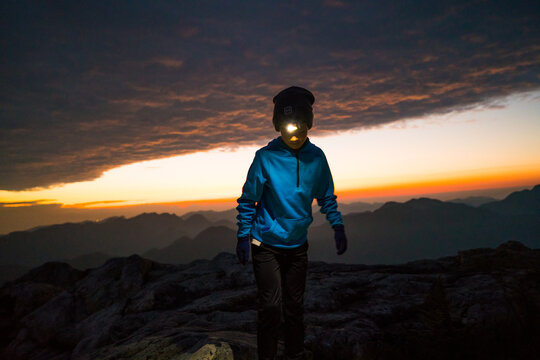 Young hiker with headlamp on mountain at sunrise