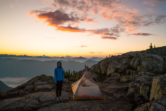 Young camper standing by a tent watching the mountain sunrise