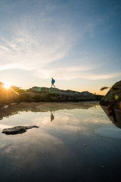 Person hikes along a rocky shore at sunset