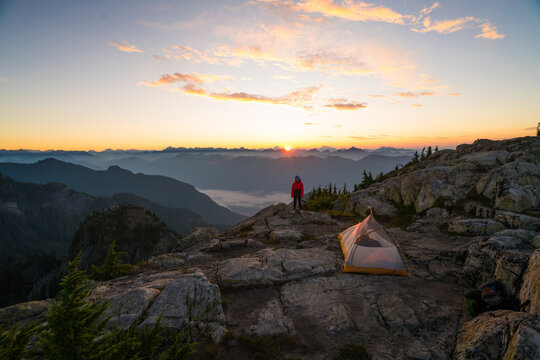 Backpacker watching sunrise from mountain peak campsite