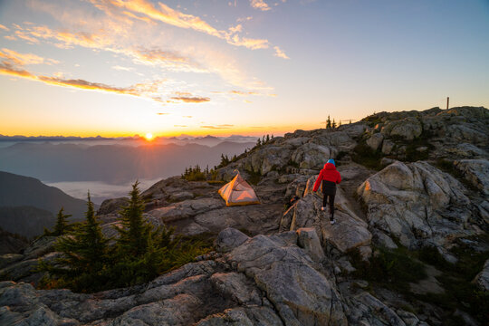 Hiker exploring mountaintop campsite at sunrise