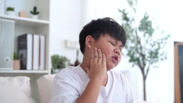 Young child experiencing toothache, tooth decay, childhood dental pain. The child facial expression, hand gently pressed against the cheek, dental care, children oral health, pediatric dental check-up
