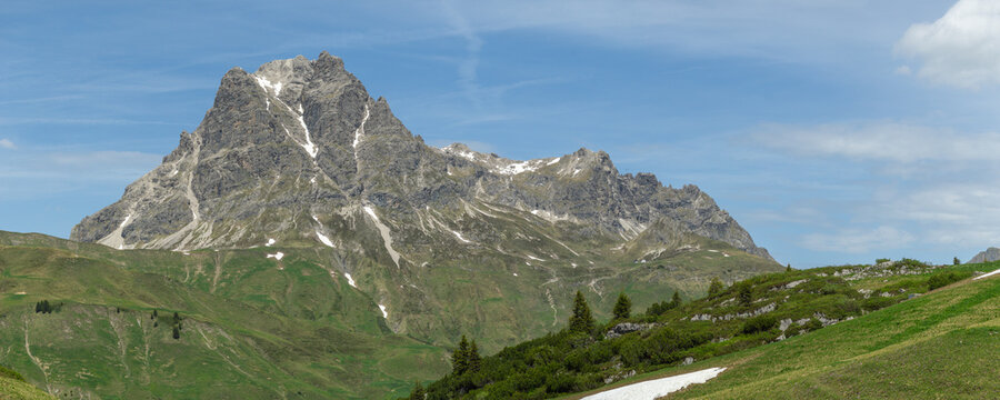 Summit Aries stone and red flowered colored meadows and K&ouml;rber lake in the alps of Bregenzerwald, with rocky mountains and steep, stony slopes on a sunny day with veil clouds.
