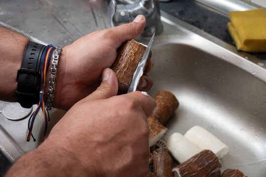 Hands peeling raw yuca cassava root vegetable in kitchen sink
