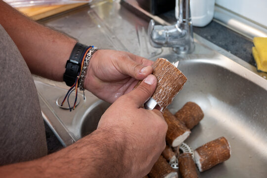 Hands peeling raw cassava, preparing yuca for cooking