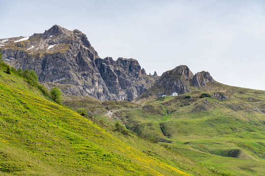 Summit Aries stone with Widdersteinh&uuml;tte and red flowered colored meadows, hiking place in the alps of Bregenzerwald, with rocky mountains and steep, stony slopes on a sunny day with veil clouds.