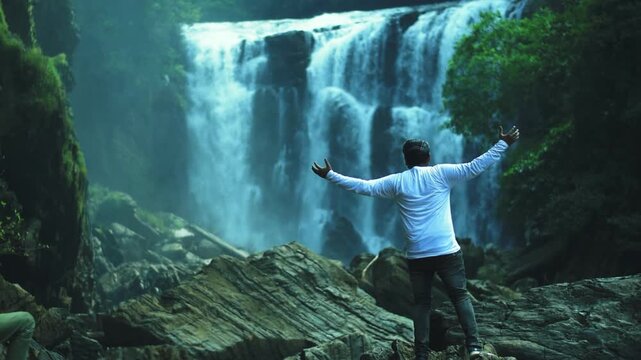 Man embraces the majestic Sathodi Waterfalls in India's Western Ghats, a breathtaking Karnataka tourism destination, symbolizing freedom and nature's grandeur.