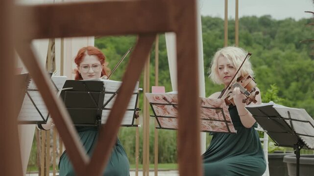 Two professional female violinists performing live classical music during an elegant outdoor event.