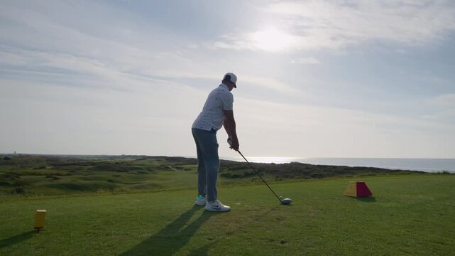 Golf driver shot swing of tee at seaside golf course, low angle slomo