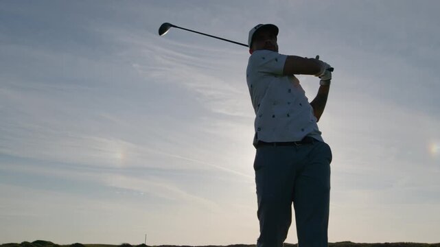 Male golfer swings driver of tee, front slomo sunset