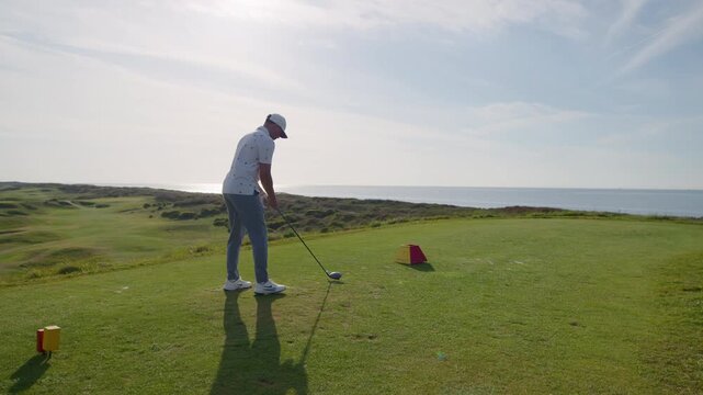 Golfer swing from tee at seaside golf course on sunny day
