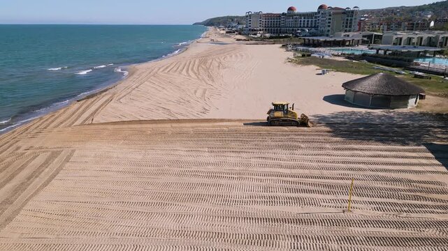 Aerial view of a bulldozer leveling and cleaning the sand on a beach resort