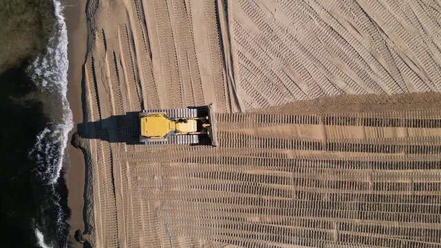 Aerial view of a bulldozer leveling and cleaning the sand on a beach resort