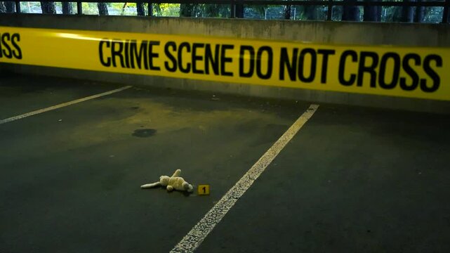 Yellow crime scene tape marking off a restricted area in an underground parking garage with a toy bunny and an evidence marker number one on the ground, suggesting a possible kidnapping