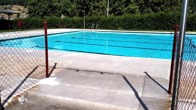 Wide shot of empty outdoor swimming pool with clear water on a sunny day