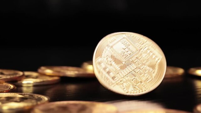 Golden bitcoin coin spinning and tumbling in slow motion on a reflective dark surface with other coins.