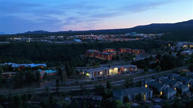 Aerial drone timelapse of the suburban town of Los Alamos, New Mexico at dusk. Evening shadows fall over the mesa as street and house lights flicker on against a deep blue twilight sky.