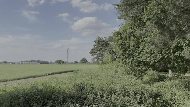 A turbine turning in the wind next to a barn on a farmer&rsquo;s field is seen through trees on a bright and sunny summer&rsquo;s day.