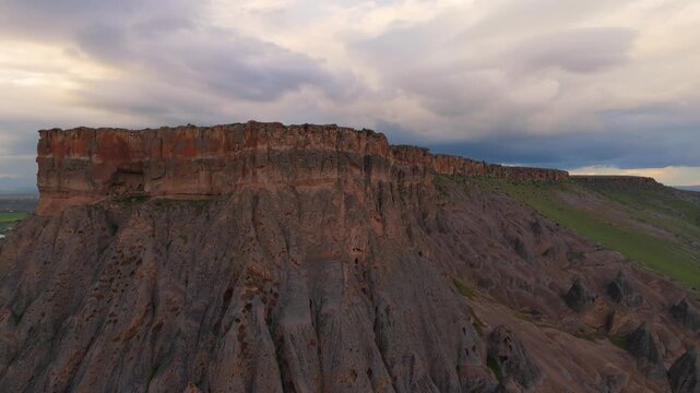 drone flyover showing the extensive geological plateau above Selime Cathedral rock monastery. Vast volcanic mountain landscape under a cloudy twilight sky in Turkey