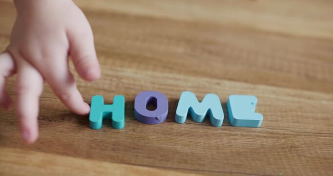 Toddler hand playing with wooden alphabet blocks spelling Home word