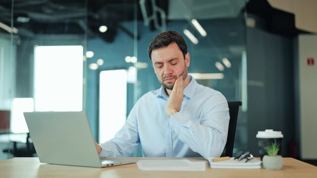 Close-up of stressed businessman or IT specialist feeling sharp dental pain or sensitive teeth at laptop. Concerned corporate manager or freelance designer suffering from bad health problem at desk