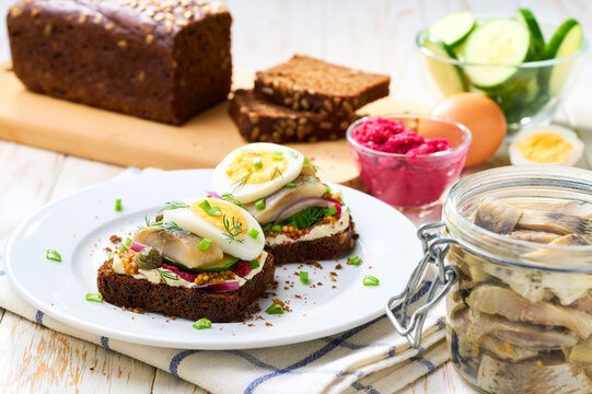 smorrebrod with rye toast bread and herring, boiling egg, red onions on wooden table, selective focus.