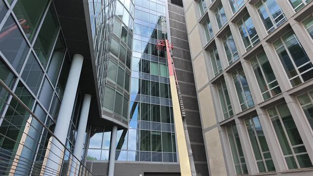 Glass window building cleaning. Industrial 4K video showing a picker crane lift basket elevated next to a modern office building glass facade for window cleaning or maintenance work.