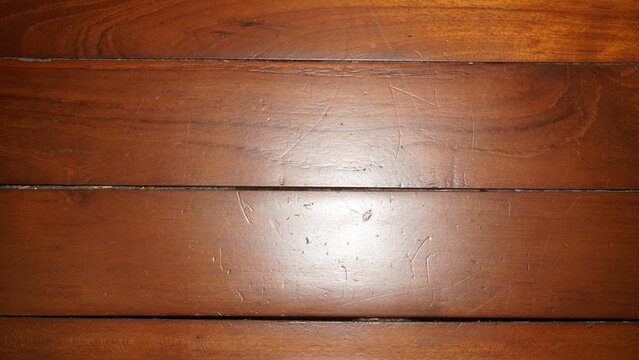 Glossy brown wooden floor panels showing natural grain texture and light reflection.