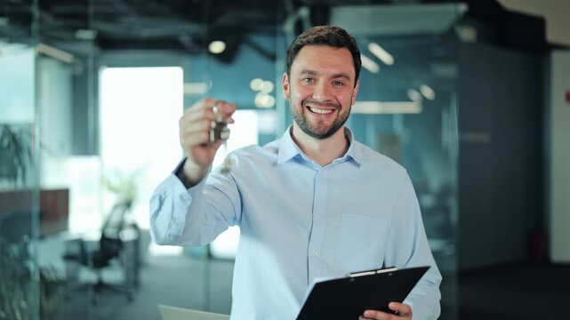 Happy real estate agent, landlord or executive holding key to commercial building or apartment. Smiling businessman or salesman showing rental deal or purchase contract inside modern office space