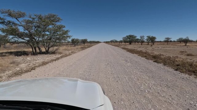 A lone white car drives along a dusty dirt road in southern Namibia, Africa.