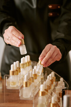 Vertical shot of young adult woman arranging perfume bottles on display, presenting beauty product assortment for retail merchandising, ecommerce or branding use